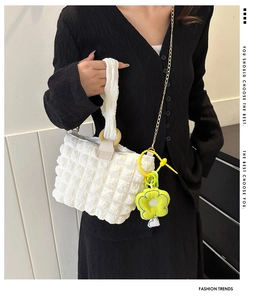 Detail view of white bubble texture bucket bag with gold chain and sunflower charm