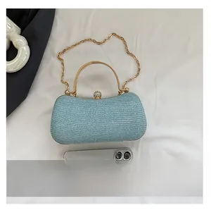 Detail view of woven blue clutch with gold top handle and diamond clasp next to phone