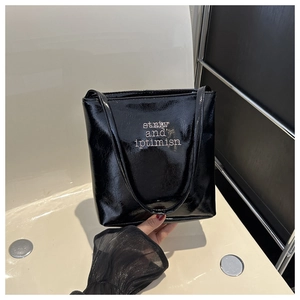 Close-up of black glossy patent leather tote bag with striv and optimism print detail