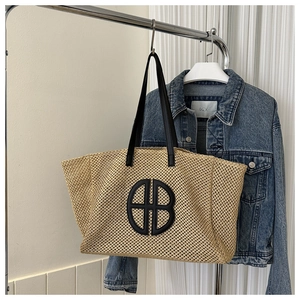 Detail of hand-woven straw tote bag with black leather shoulder straps and round logo