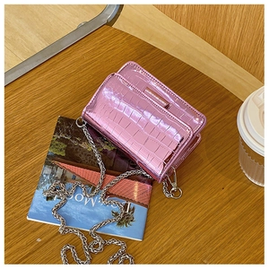 Close-up of pink crocodile texture crossbody bag with silver chain on a cafe table