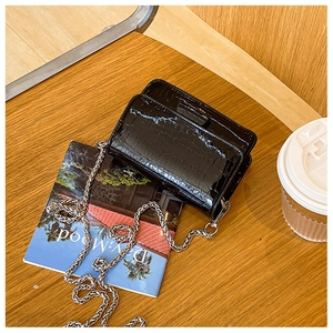 Detail of black crocodile texture bag with silver chain on a wooden table setup