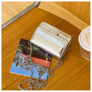 Close-up of metallic silver crocodile-texture crossbody bag with silver chain on wood