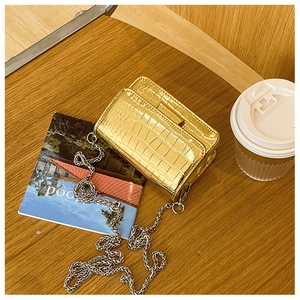 Close-up of golden croc-effect crossbody bag with silver chain on a modern desk