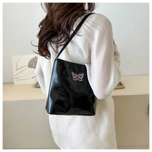 Detail of black glossy leather bucket bag featuring pink butterfly embroidery on strap