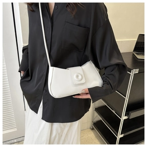 Close-up of minimalist white square crossbody bag with unique round buckle detail on a model
