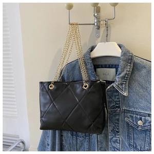Détail d'un sac bandoulière matelassé noir avec chaîne dorée sur une veste en jean
