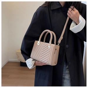 Detail of beige quilted handbag with double woven handles and gold-tone hardware on model