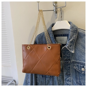 Détail du sac cabas matelassé marron avec chaîne dorée sur fond en jean bleu