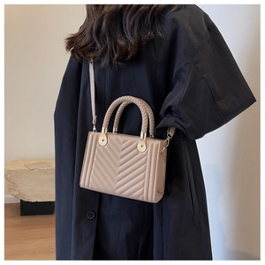Detail of beige plaid crossbody bag with braided handle worn by model on black coat