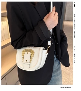 Close-up of white leather saddle bag with ornate gold buckle on model with black blazer
