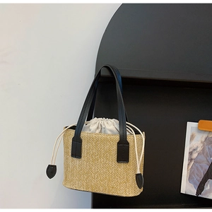 Detail of handwoven straw bag featuring herringbone texture and black leather handles