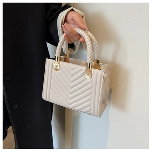 Detail of cream quilted handbag featuring woven top handle and gold-tone metal hardware