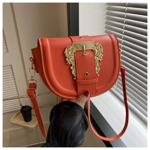Macro shot of orange saddle bag with large gold baroque buckle and matte leather texture