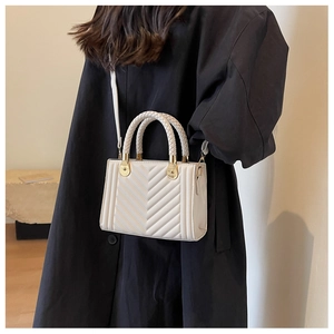 Fashionable white quilted crossbody bag with woven handle shown on model in black coat