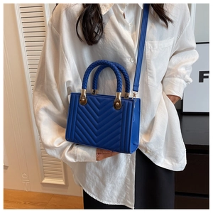 Royal blue crossbody bag with V-quilted stitching and braided handle shown on a model