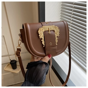 Detail view of brown saddle bag featuring an ornate golden baroque embossed buckle