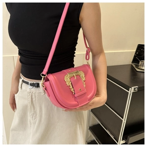 Pink saddle bag featuring a decorative golden baroque buckle worn by a model in lifestyle setting
