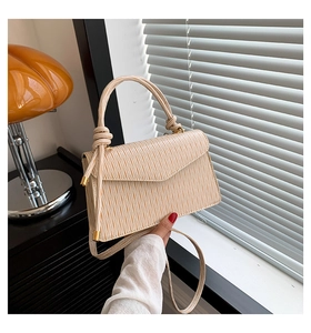 Détail d'un sac à main plissé beige avec poignée nouée et finitions métalliques dorées