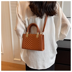 Detail of caramel quilted leather bag with woven handle and gold hardware on a model