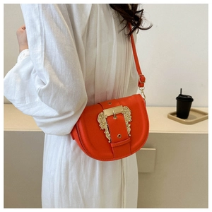 Detail of a bright orange saddle bag with gold Baroque buckle worn on a white dress