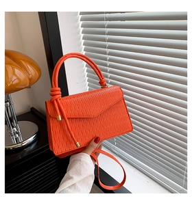 Détail d'un petit sac carré orange vif plissé avec poignée à boule métallique et bandoulière