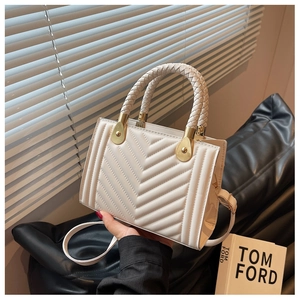 Detail of cream plaid handbag with V-stitch texture, woven handles and gold metal accents