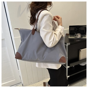Detail der grauen Oxford-Stofftasche mit braunen Ledergriffen, getragen von einem Modell