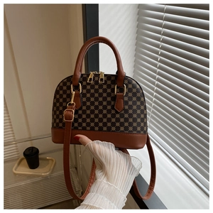 Detail van een bruine schelpvormige crossbodytas met vintage geometrisch patroon en goudaccent