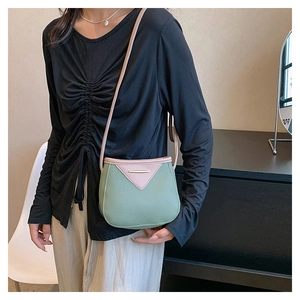 Detail of green lychee leather crossbody bag with pink trim and metal accents on model