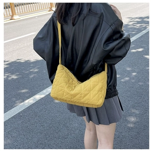 Detailed view of yellow quilted dumpling bag with wide shoulder strap worn by a model