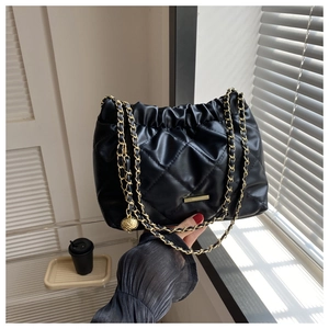 Detail of black quilted crossbody bag with golden chain strap and metallic sphere charm