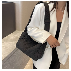 Detail of black quilted shoulder bag with adjustable wide strap shown on a model