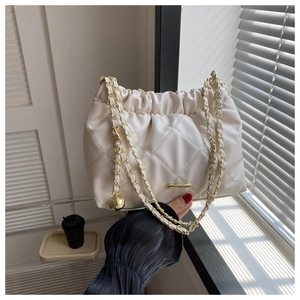 Detail of beige quilted crossbody bag with gold chain strap and metal ball decoration