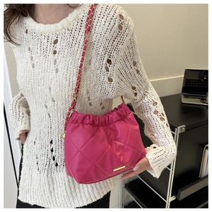 Detail of fuchsia quilted bucket bag with gold chain strap worn over the shoulder
