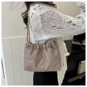 Sac seau matelassé beige avec chaîne dorée porté sur un pull en maille blanche