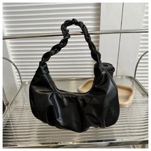 Detail of black pleated cloud bag with a unique woven strap on a glass shelf