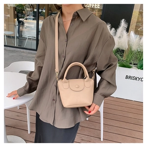 Close-up of beige lychee grain leather bucket bag with top handle and magnetic snap closure