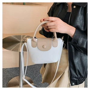 Detail of white PU leather mini bucket bag with beige handles held by fashion model