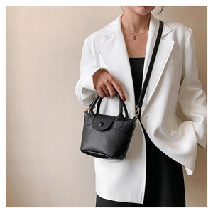 Detail of black lychee texture PU bucket bag with golden hardware on a white blazer