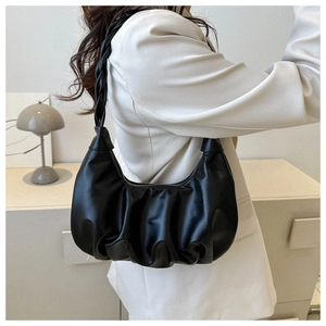 Detail of black pleated cloud bag with a braided shoulder strap in a minimalist setting