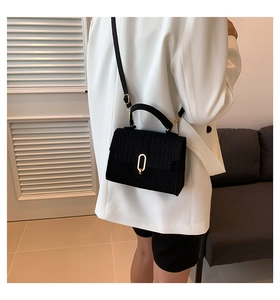 Detailed view of crocodile embossed black crossbody bag with golden oval twist lock