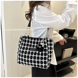 Side view of model wearing a black and white plaid tweed tote bag with chain strap