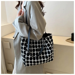 Detail of checkered tote bag with leather strap worn over a grey blazer for daily commute