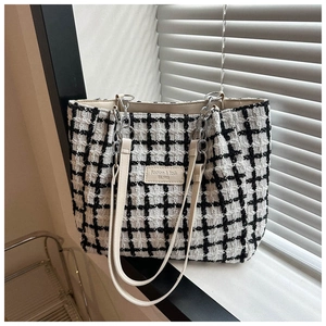 Detail of black and white tweed tote bag featuring leather label and metal chain strap