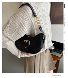 Detail of black crescent shoulder bag with large gold buckle and metal chain strap