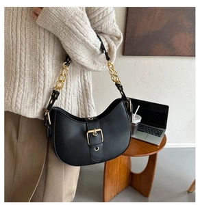 Close-up of black leather shoulder bag with gold buckle on a stylish model