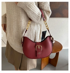 Detail of dark red half-moon bag with gold metal buckle and leather chain strap