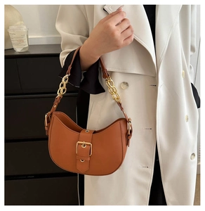 Close-up of brown crescent hobo bag with gold buckle and chain strap on white coat