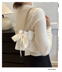 Detail of white quilted crossbody bag featuring silk bow and gold chain strap on model